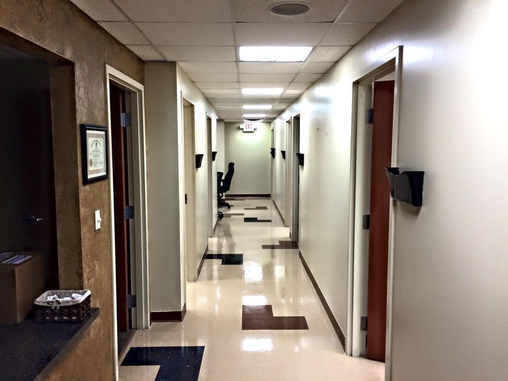 Hallway with several closed doors and black wall-mounted magazine holders. Tile floor and neutral-colored walls.