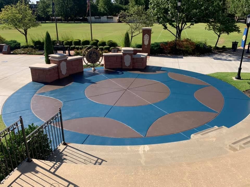 Blue and brown concrete circle design in a park, with brick structures and a decorative metal globe.