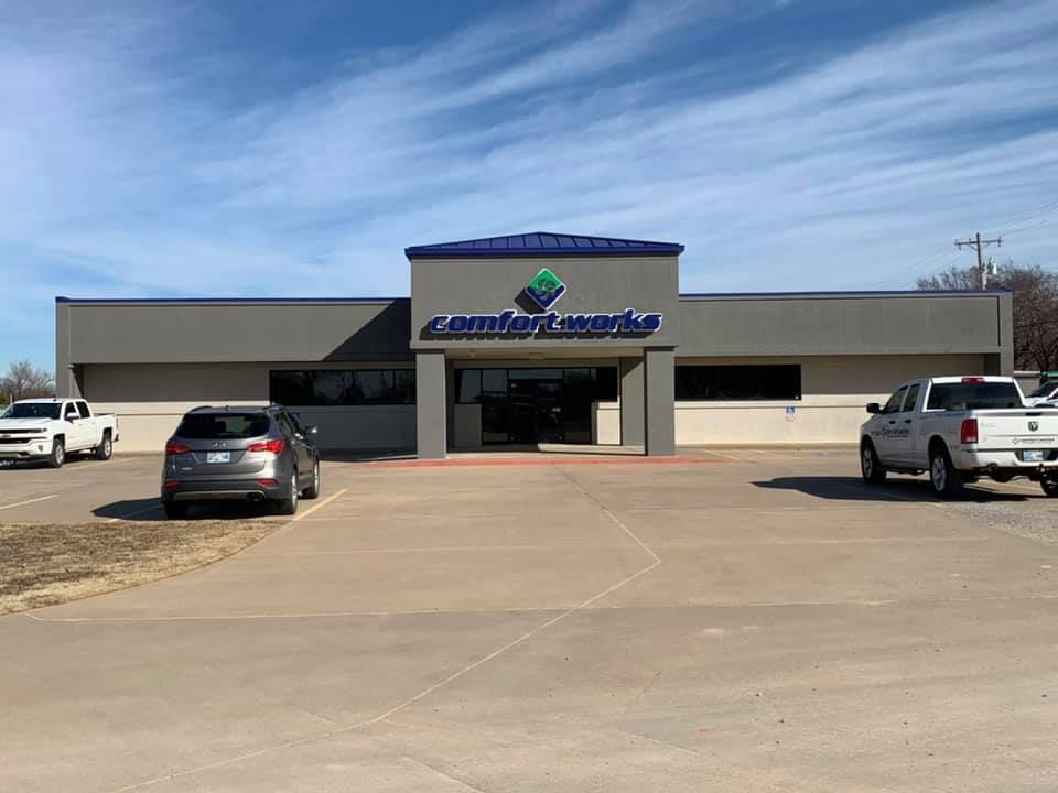 Exterior view of Comfortworks building with blue roof and logo, cars parked in front, and a blue sky.