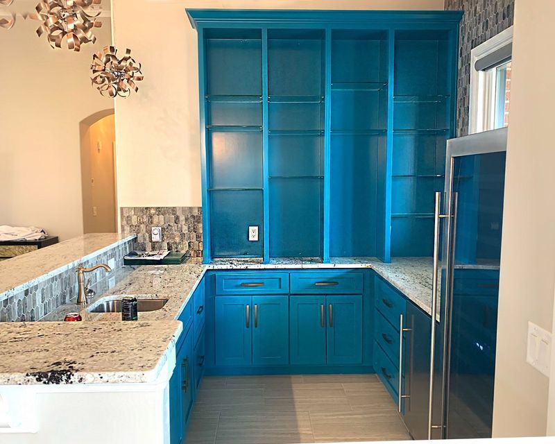 Bright blue kitchen cabinetry with granite countertops. Stainless steel refrigerator, shelves, and sink.