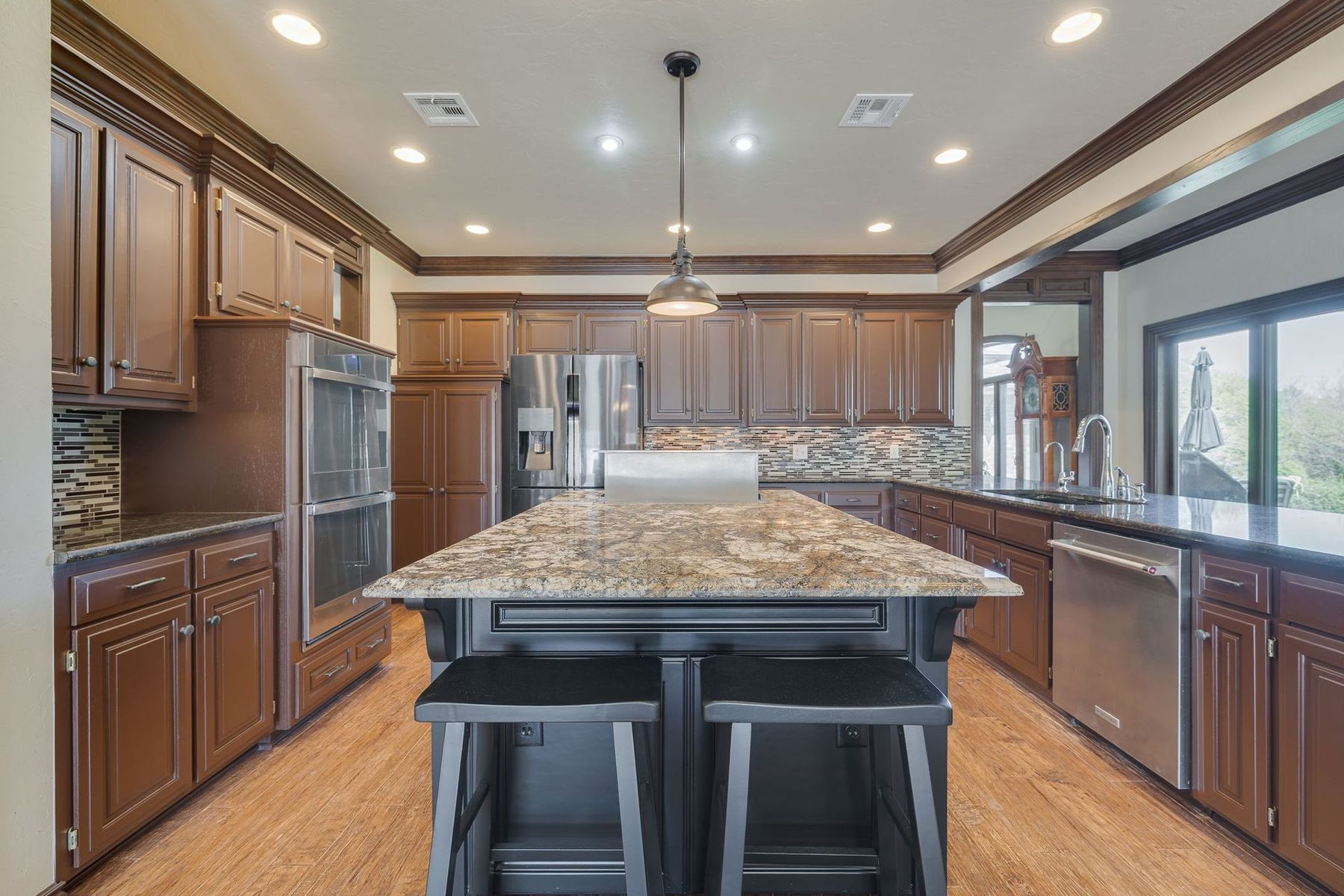 Kitchen with dark brown cabinets, large island with granite countertop, stainless steel appliances, and wooden floors.