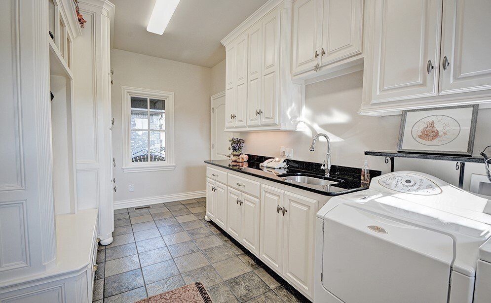 Laundry room with white cabinets, dark countertop, washing machine, window, and gray tiled floor.