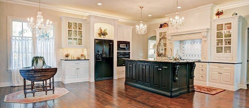 Elegant kitchen with chandelier, black island, white cabinets, and dark wood floors.