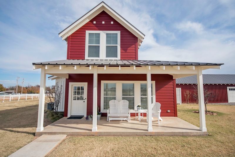 Red two-story house with white trim and a porch, set in a grassy yard under a blue sky.