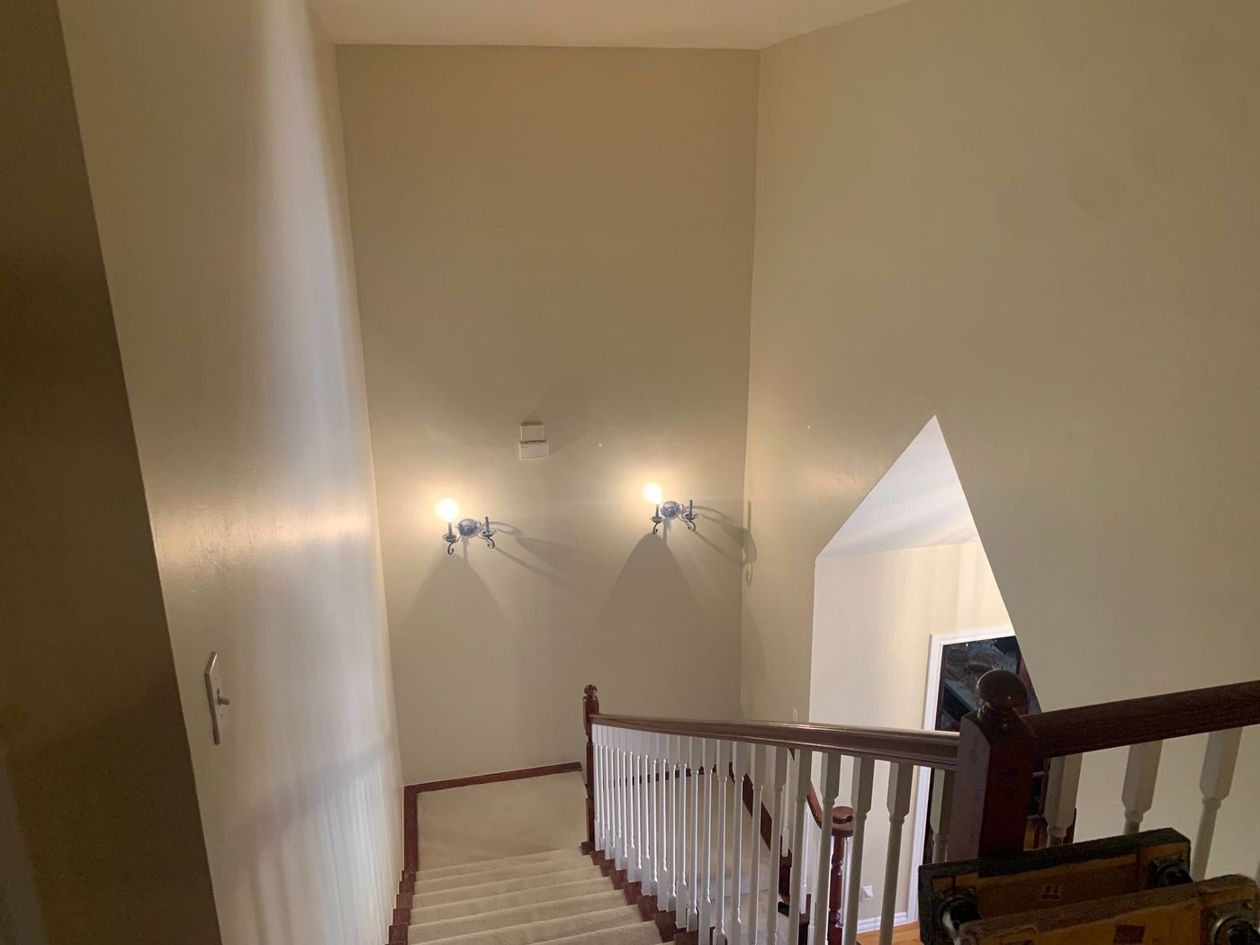 Stairwell with beige walls, sconce lights, and a wooden handrail.
