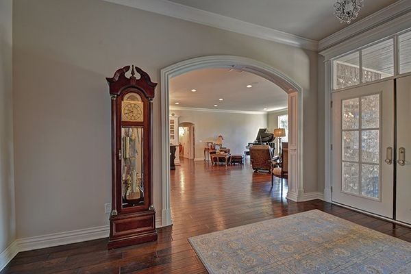 Grandfather clock in a hallway with an arched doorway leading to a living room, hardwood floors, and a rug.