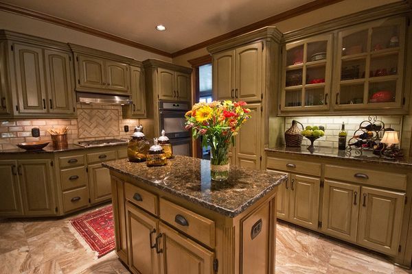 Kitchen with olive green cabinets, granite countertops, and a flower arrangement.