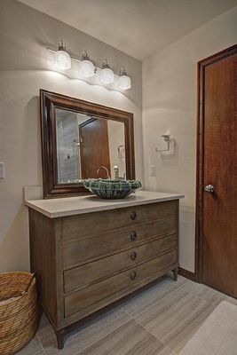 Bathroom with wooden vanity, green bowl sink, large mirror, and wall sconces.
