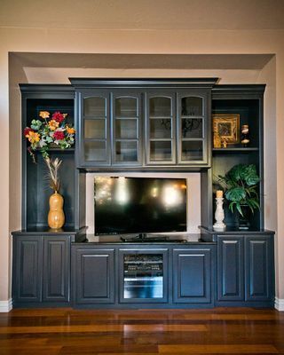 Built-in dark gray entertainment center with TV, glass-door cabinets, and display shelves in a recessed wall.
