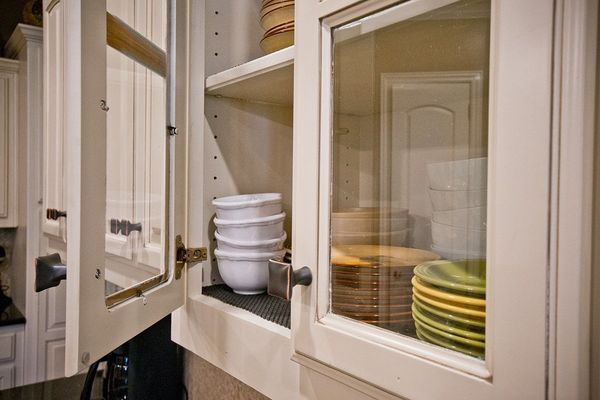 Kitchen cabinet with glass door; dishes stacked inside, open door to the left.