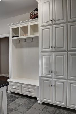 White built-in storage unit with cabinets, hooks, bench, and drawers against a white wall.