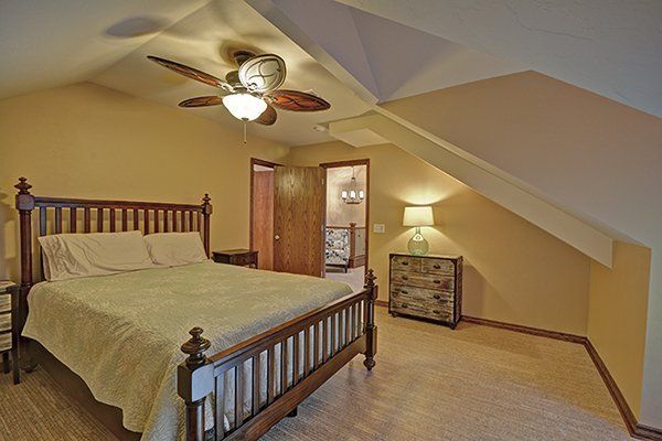 Bedroom with wood bed frame, beige walls, and sloped ceiling. A chest and lamp are visible.