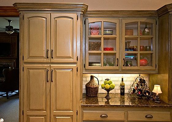 Cream-colored kitchen cabinets with glass-fronted upper cabinets. Brown granite countertop with decor.