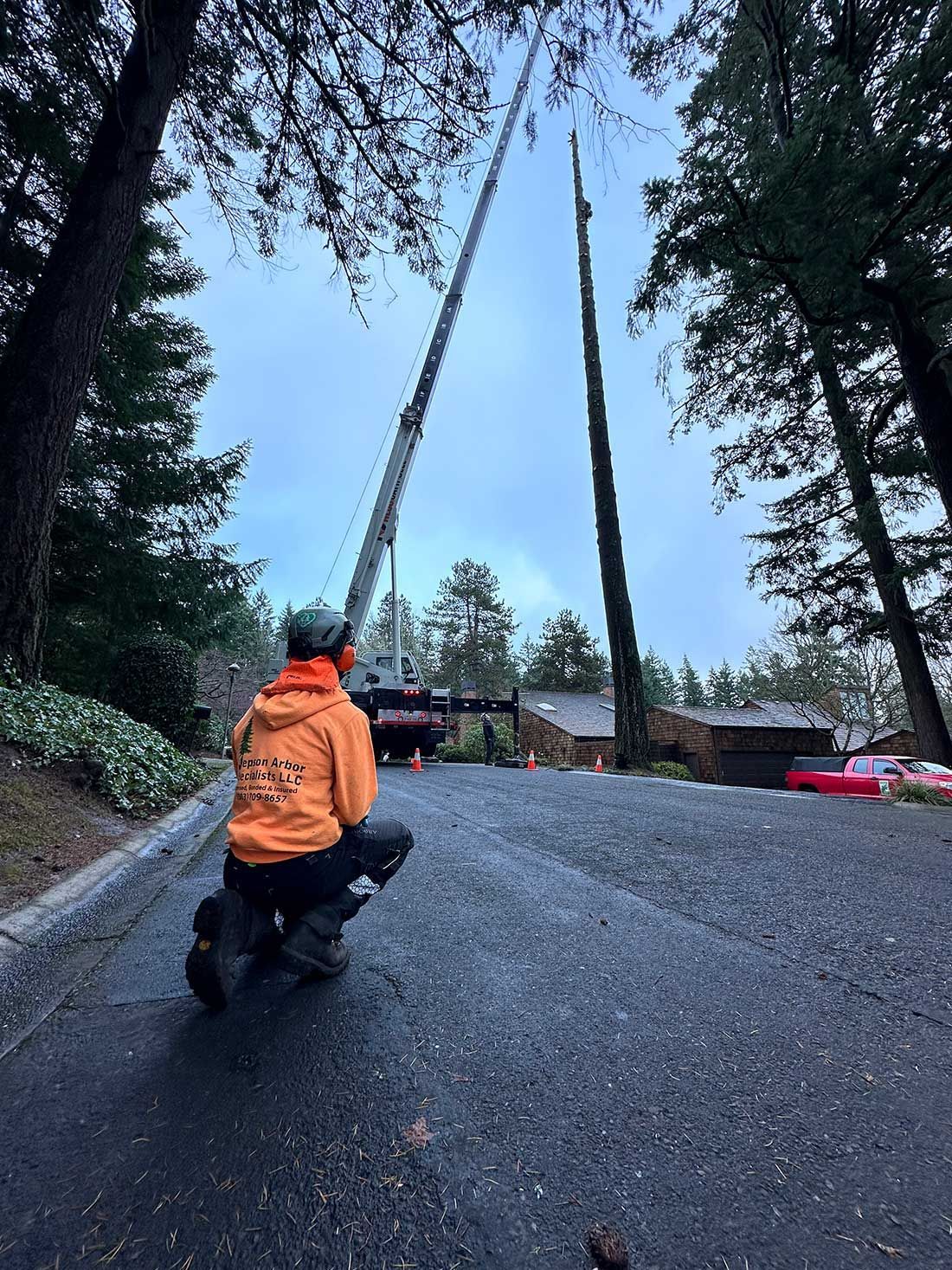 A man in an orange jacket is kneeling down in front of a large crane.
