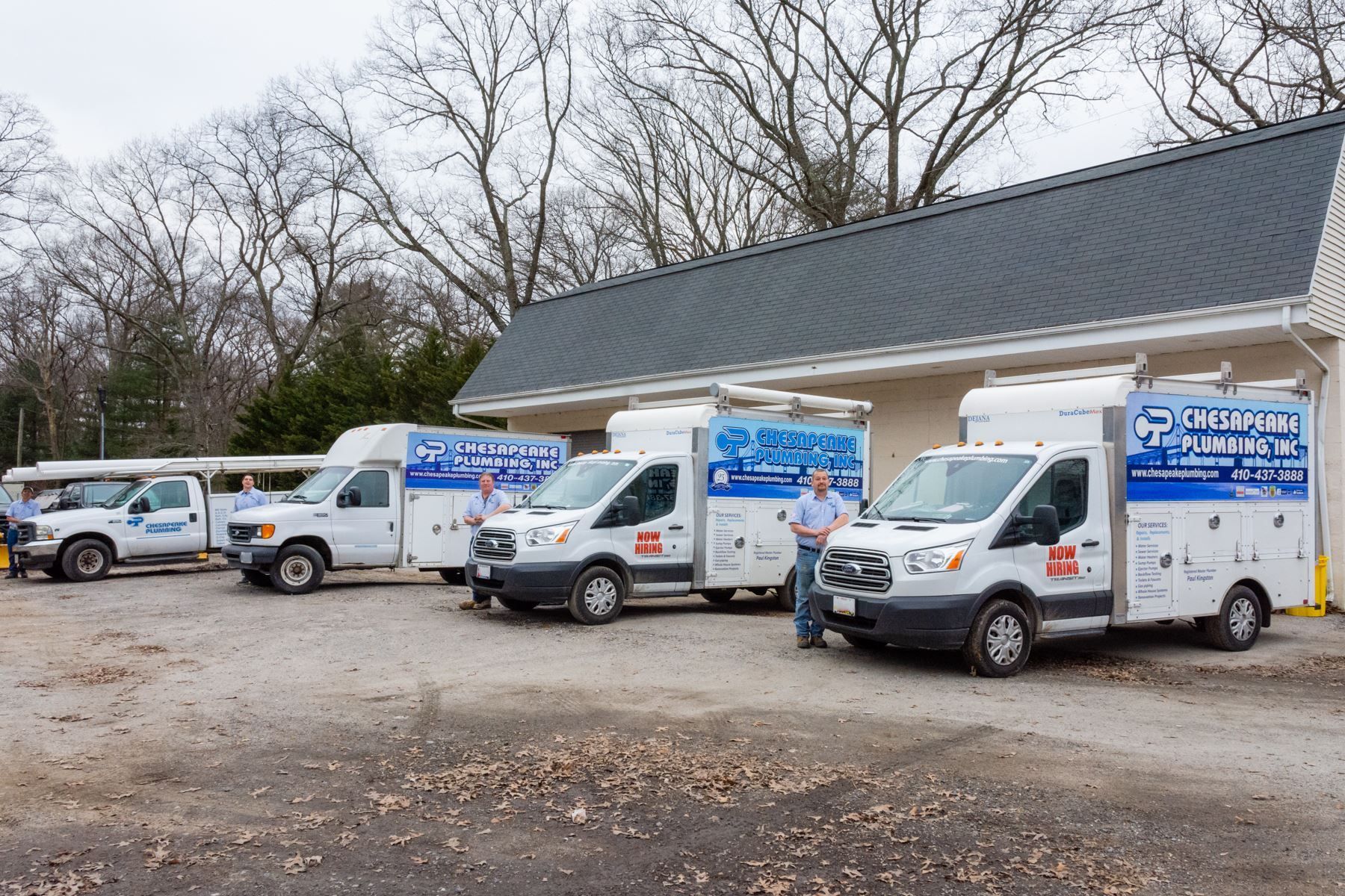 Several white service vans parked outside a building. Two men stand beside vans, possibly technicians.