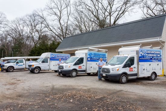 Service vehicles parked in front of a building. Two men stand beside vans with business logos. Cloudy day.