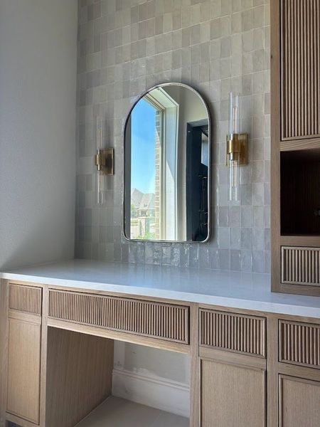 Vanity area with arched mirror, sconces, wood cabinets, and tile backsplash.