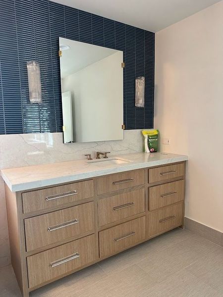 Bathroom vanity with blue tiled wall, large mirror, and light wood cabinetry with silver hardware.