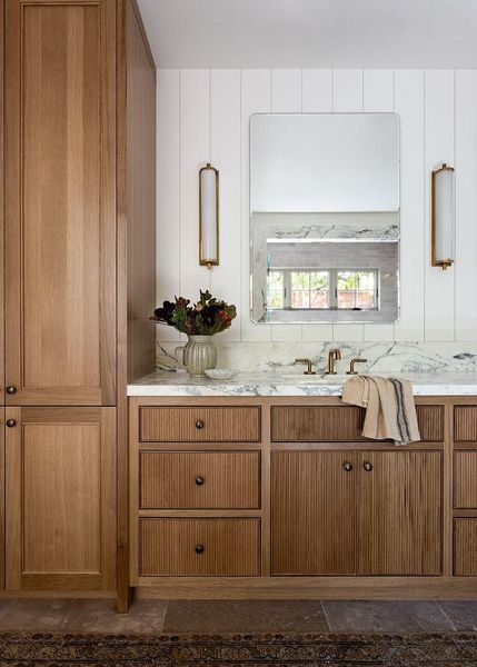 Bathroom with light wood cabinetry, marble countertop, large mirror, and sconces on white shiplap.