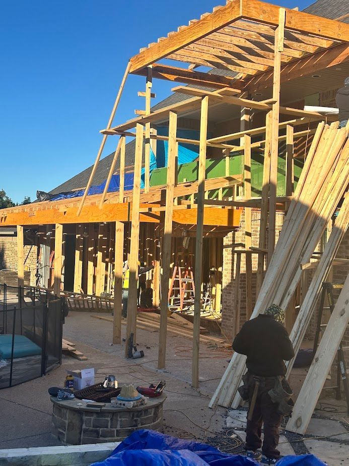 Interior of a room with folding black doors to a deck. Light wood flooring, white walls, and construction materials are visible.