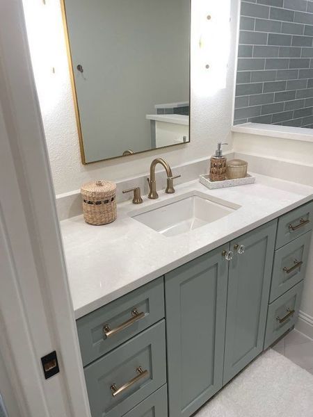 Bathroom vanity with light blue cabinets, white countertop, gold fixtures, and rectangular mirror.