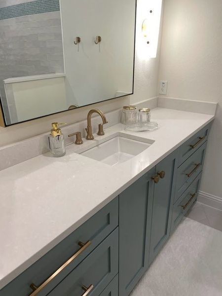 Bathroom vanity with a blue cabinet, white countertop, gold fixtures, and a large mirror.