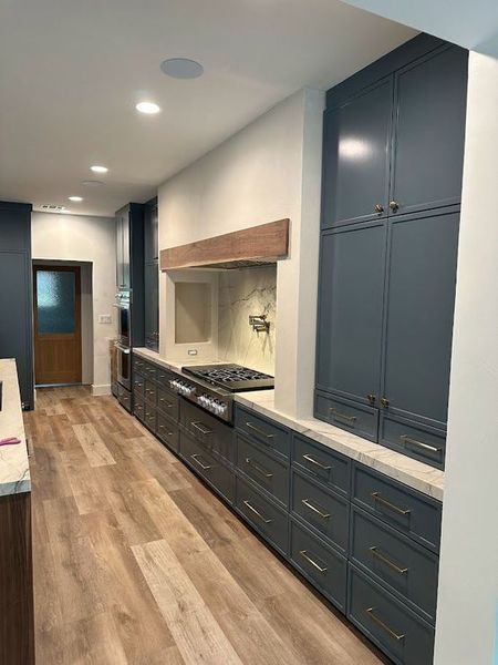 Long, narrow kitchen with gray cabinets, wooden floors, and a stone countertop.
