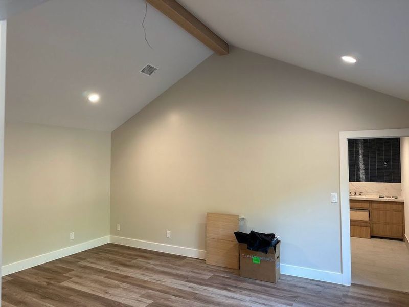 Empty room with wood-look flooring, beige walls, and white trim. Recessed lighting and a wood beam are in the high ceiling.