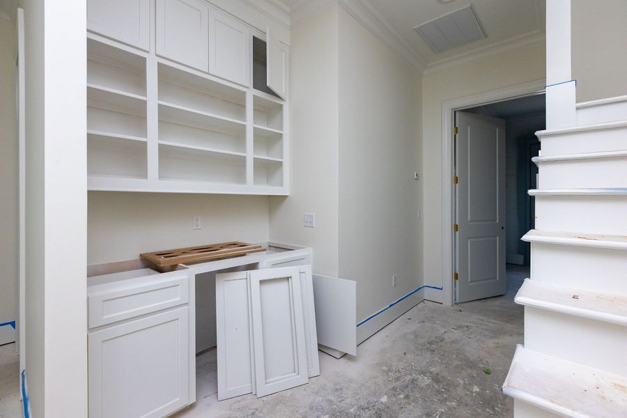 White built-in shelves and cabinets in a room with a door and stairs under construction.