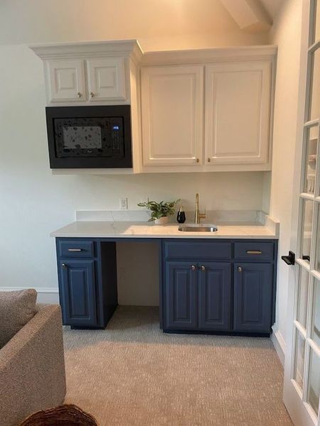 A home bar area with white and navy blue cabinets, a microwave, and a small sink.