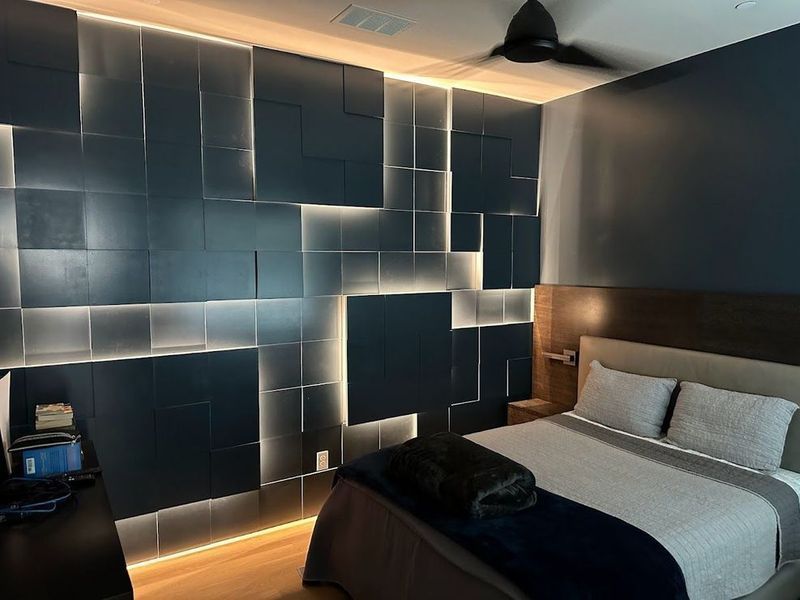 Bedroom with a dark blue textured wall, inset lighting, and a bed with blue and gray bedding.