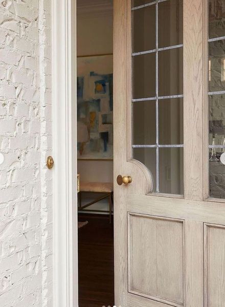 White brick wall and partially open wooden door with glass panels. View into a room.