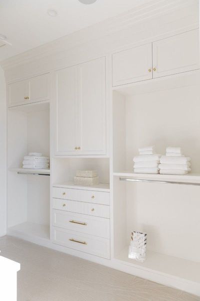 White built-in storage closet with drawers, shelves, and folded towels. Gold hardware accents.