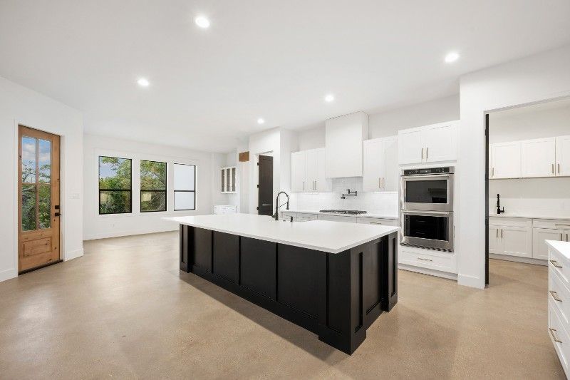 Modern white kitchen with black island, white countertops, and stainless steel appliances.