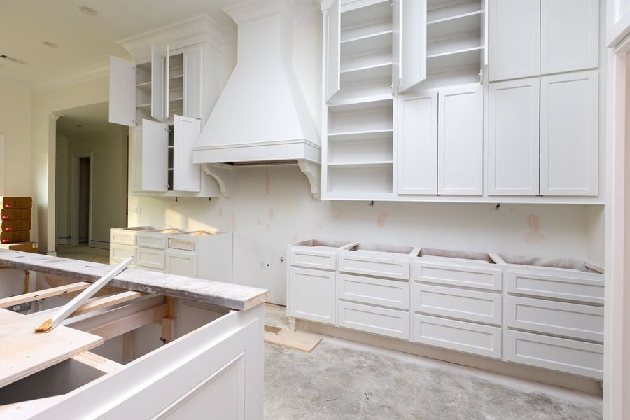 Kitchen cabinets being installed, with a range hood and open doors in a room under construction.