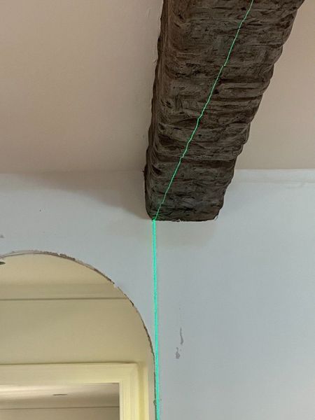 A stone beam spans above a white wall with an arched doorway. A vertical green line is projected.