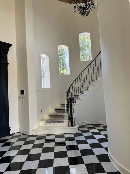 Black and white checkered floor, curved staircase with wrought iron railing, arched windows, chandelier.