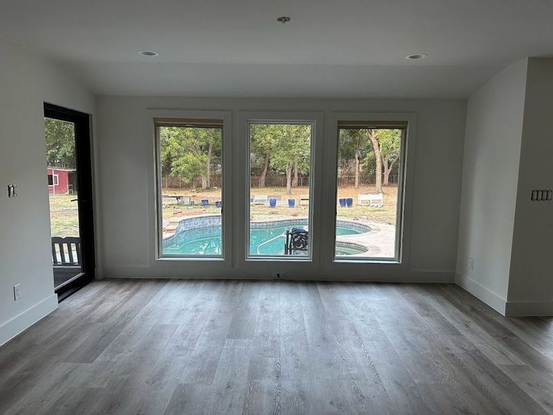 Interior room with large windows overlooking a pool and yard, with gray flooring and a black door.