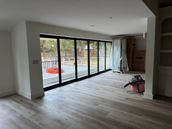 Interior of a room with large black framed folding glass doors leading to a wooden deck. Gray flooring and white walls.