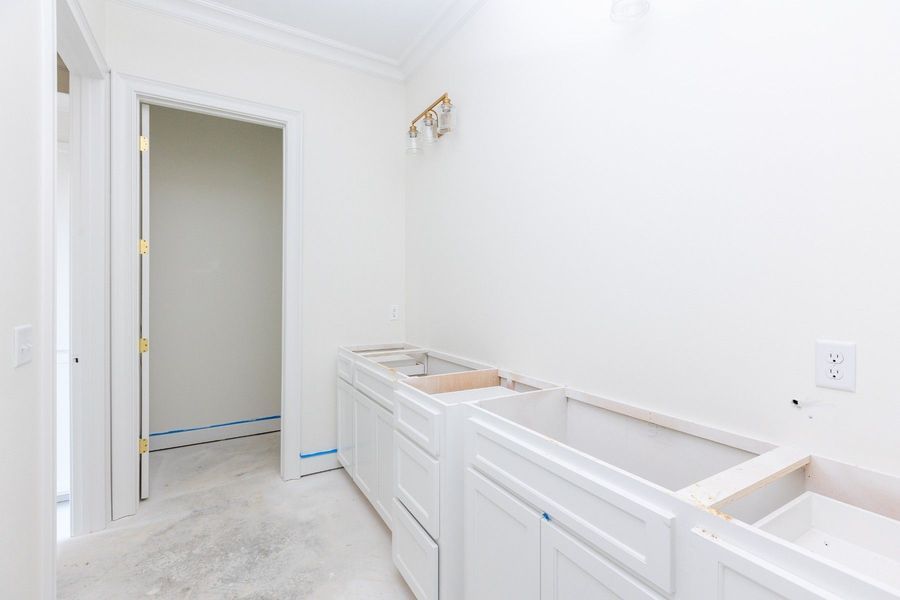 Bathroom renovation in progress with white cabinets, walls, and an open doorway.