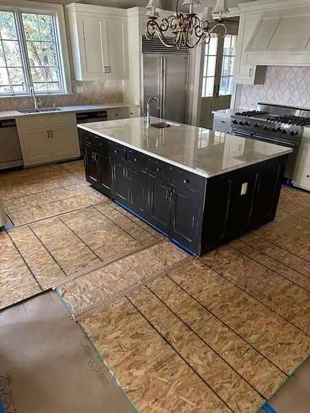 Kitchen with black island, white cabinets, and unfinished wood flooring, awaiting installation.