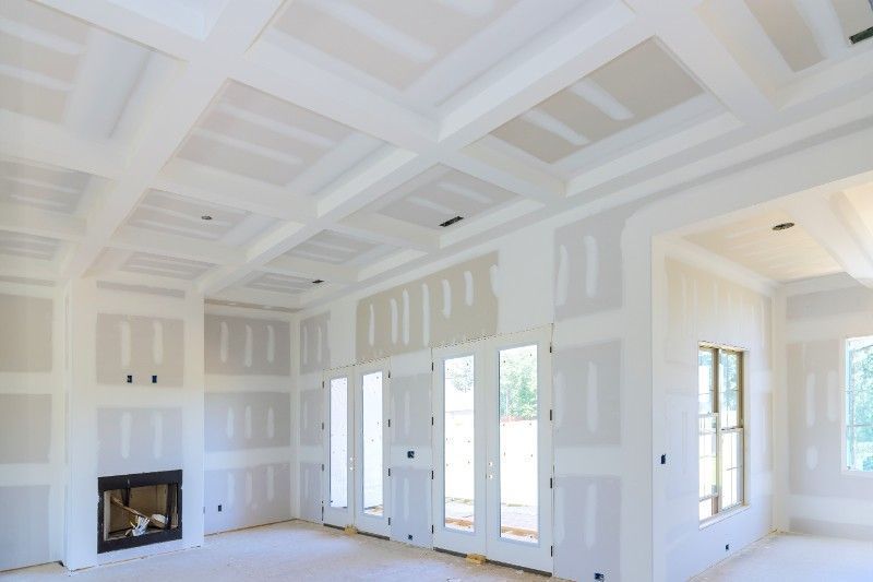 Interior of a room under construction, with drywall on walls and ceiling. Fireplace and doors are visible.