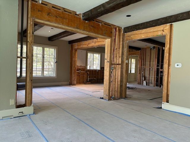Interior view of a room under construction with exposed wooden beams, doorways, and unfinished floors.