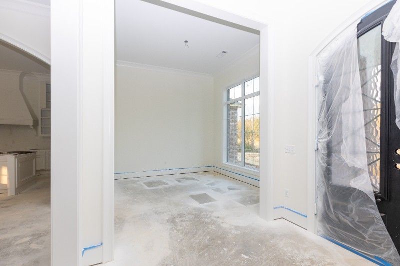 Interior of a house under construction; white walls, bare concrete floor, and plastic-covered door.