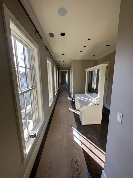 Long hallway with windows on one side and a built-in vanity at the end. Wooden floors and neutral-colored walls.