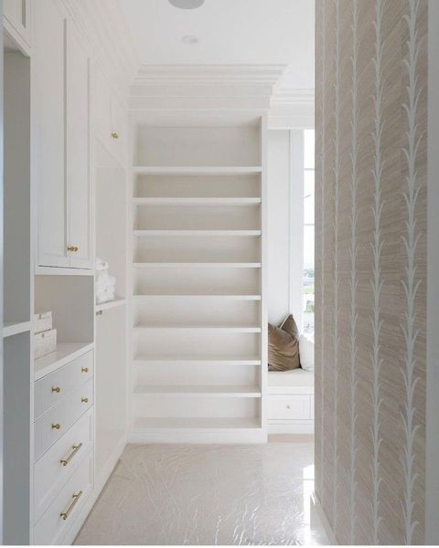 White built-in shelves and cabinets in a room with patterned wallpaper, window seat, and gold hardware.