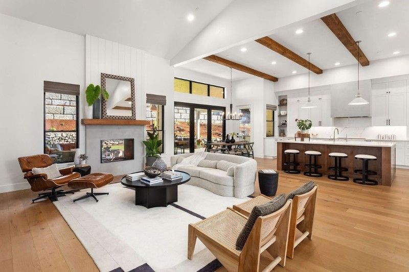Modern living room with a fireplace, open kitchen, and light-colored wood flooring.