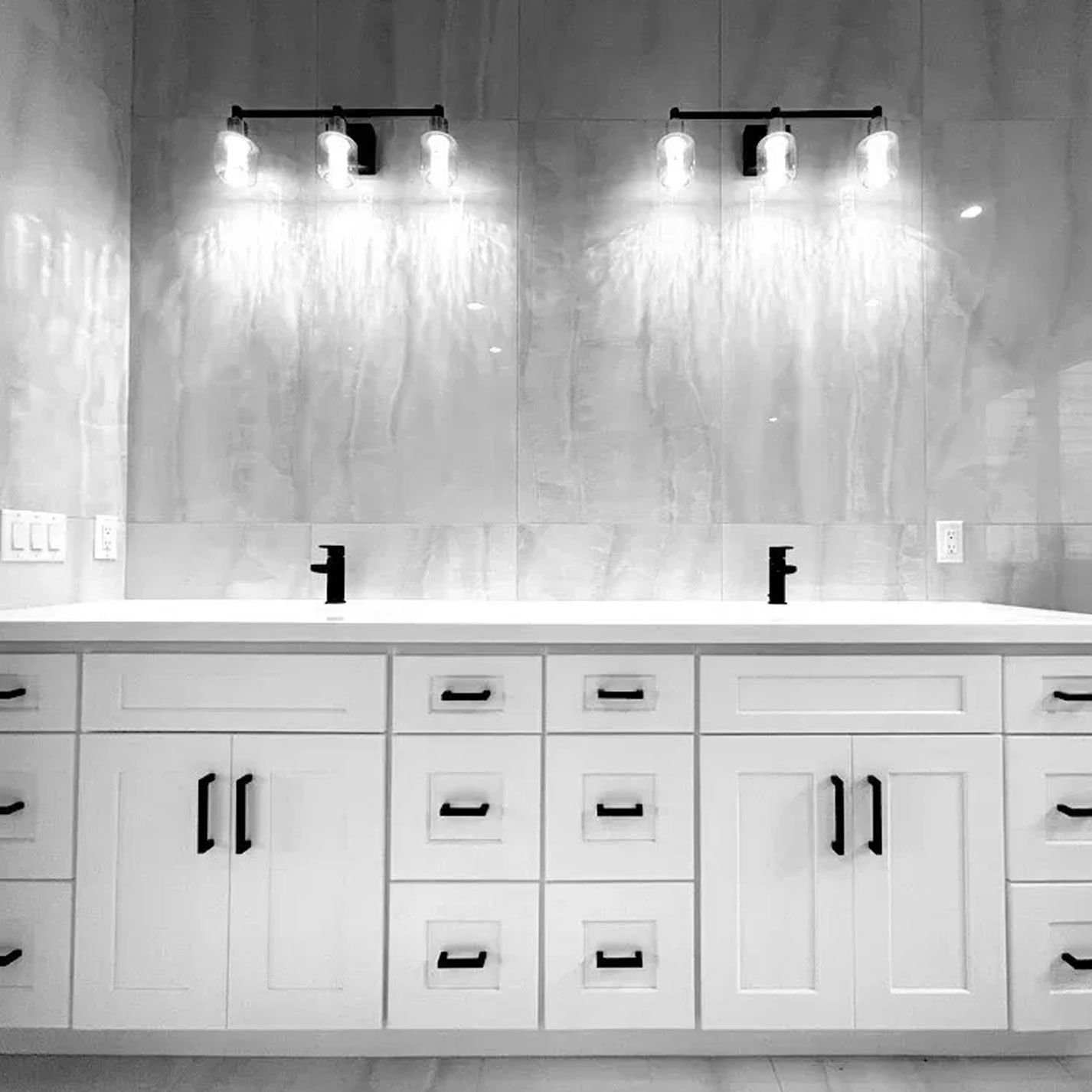 A black and white photo of a bathroom with two sinks and cabinets.