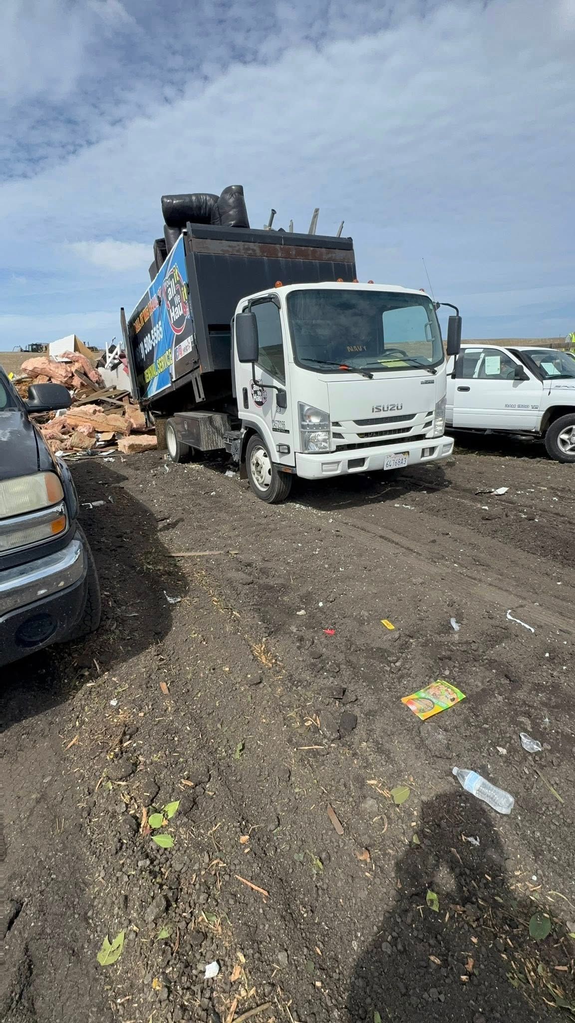 A white garbage truck dumping trash at a landfill on a cloudy day.