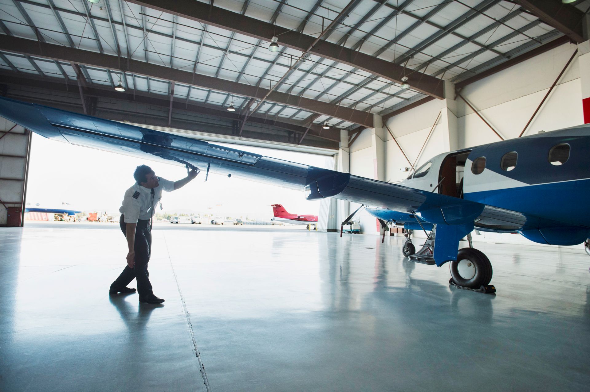 A person inspecting the wing of a blue and white airplane inside a hangar.